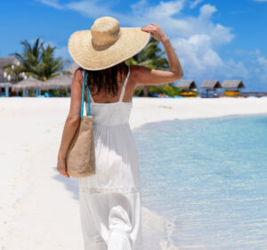 Arm Lift model holding her hat while walking on beach in Florida